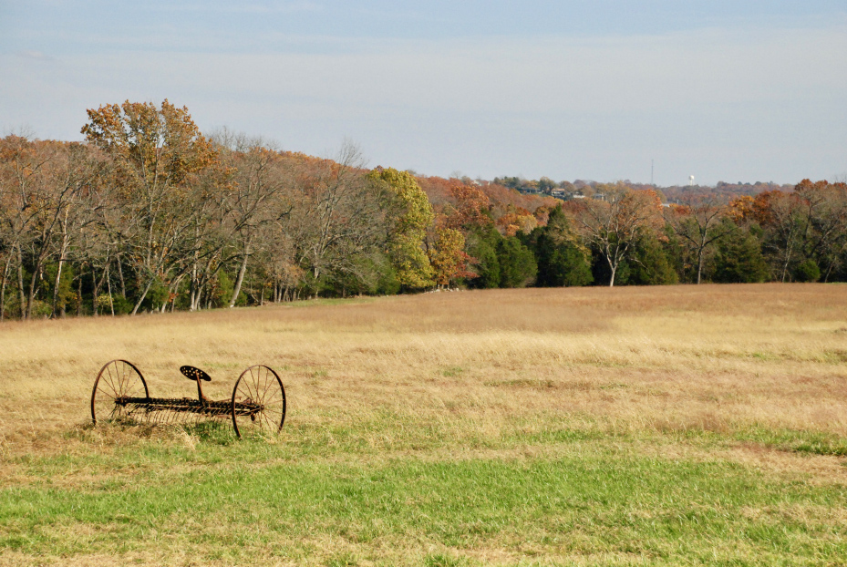 Open field with vintage farm equipment and fall trees at Homestead Farm Retreat & RV in Branson, Missouri